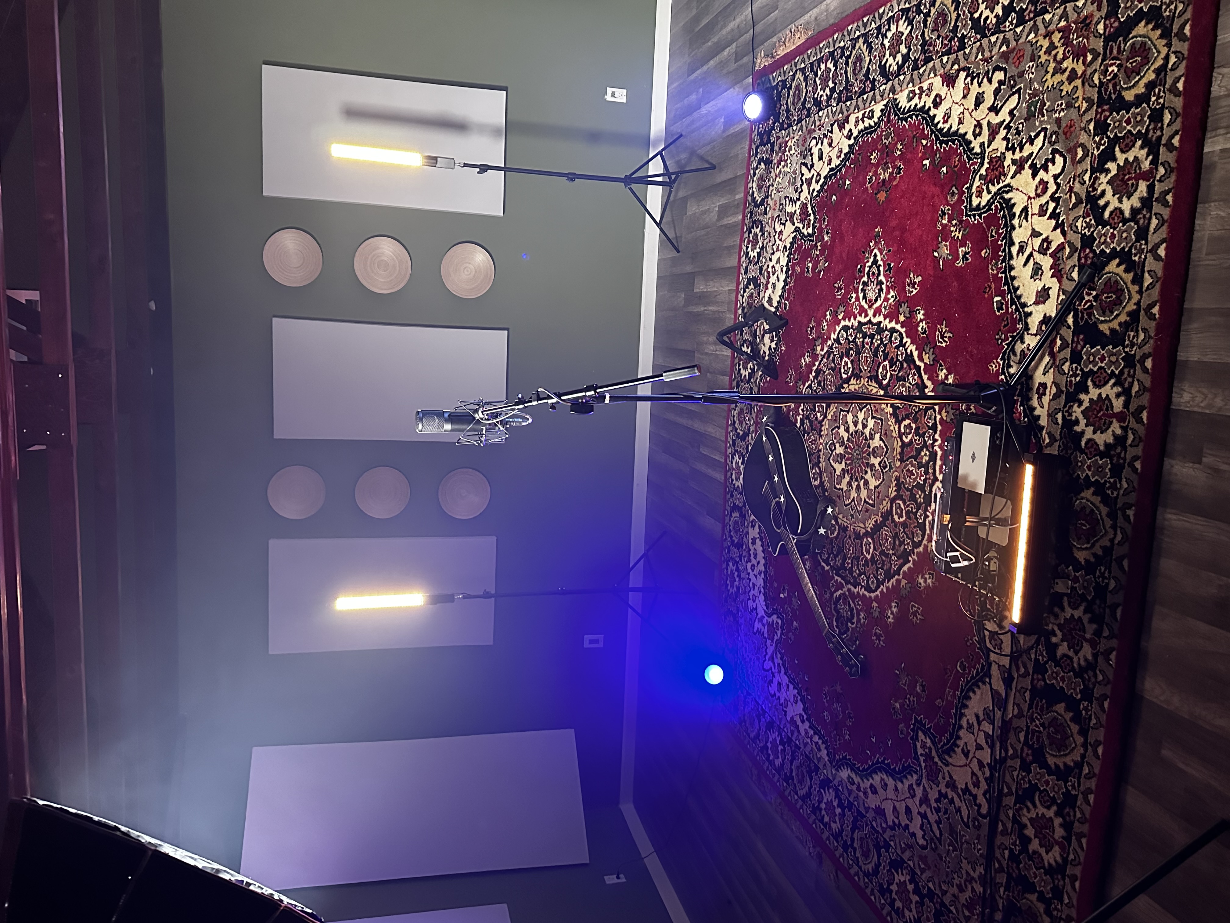 Acoustic guitar and vocal microphone set up on a rug under studio production lights