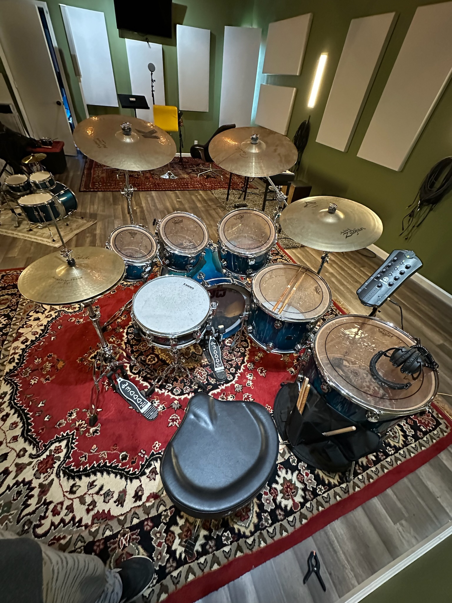 Full drum kit and cymbals on a patterned rug, surrounded by live-room acoustic panels